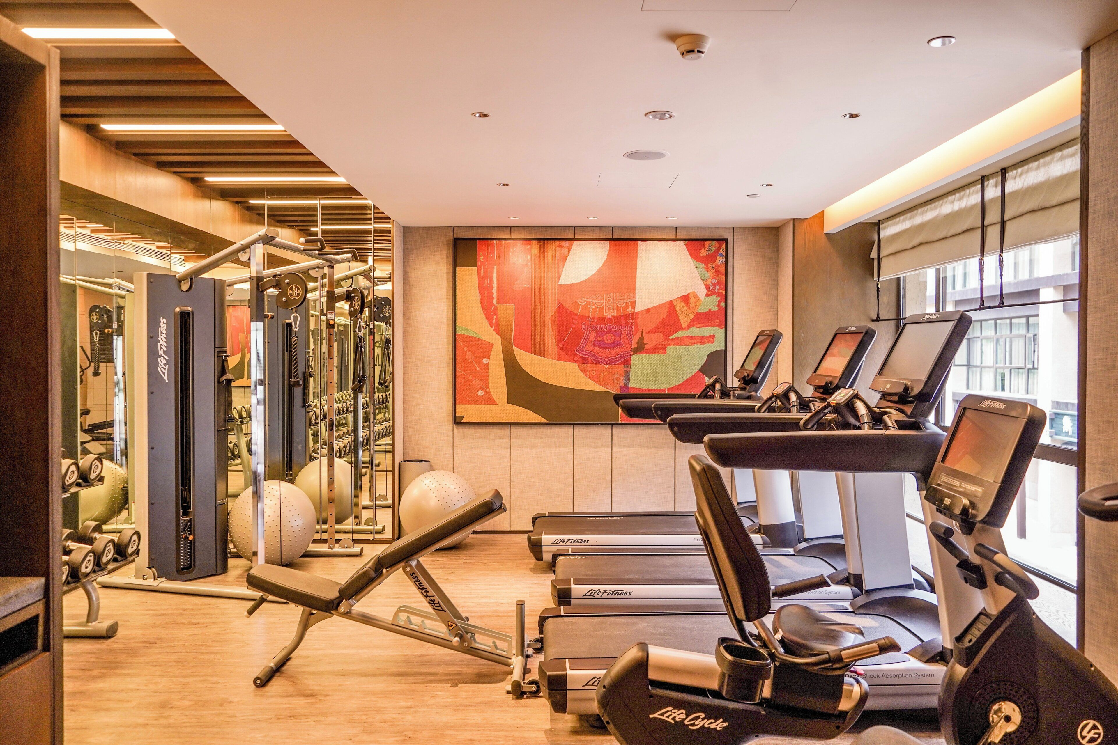A gym with cardio equipment, weight machines, and a large abstract painting on the wall.