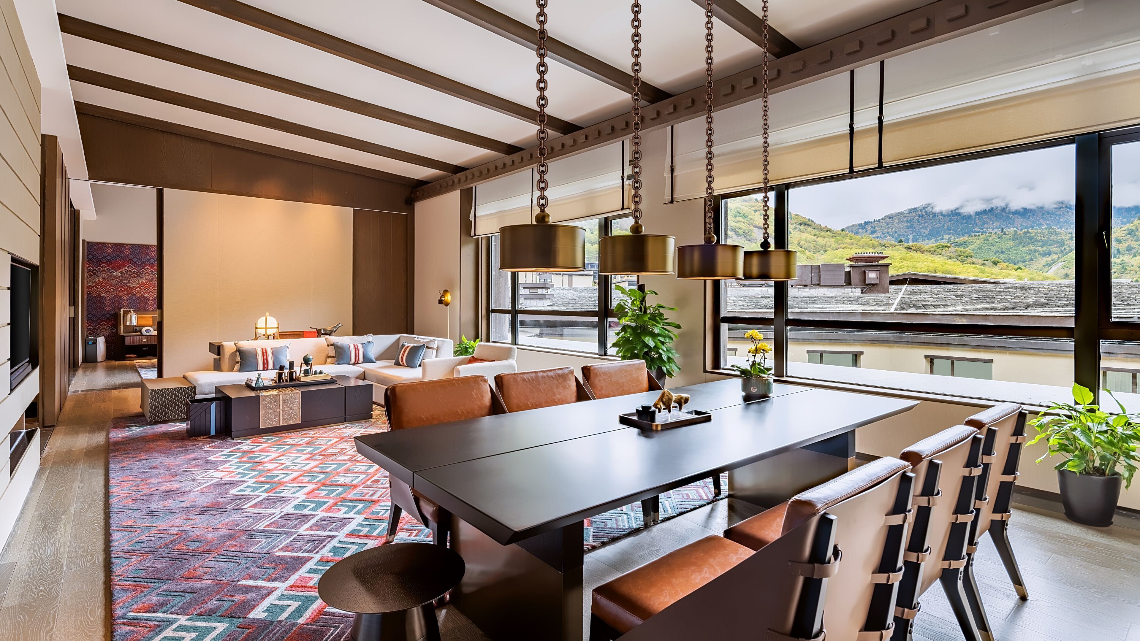 A modern living space with a dining area, a sofa set, and a large window offering a mountain view.