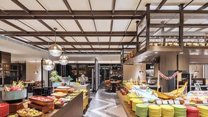 A spacious hotel lobby with a high ceiling, modern lighting fixtures, and a central area with food and beverage service.