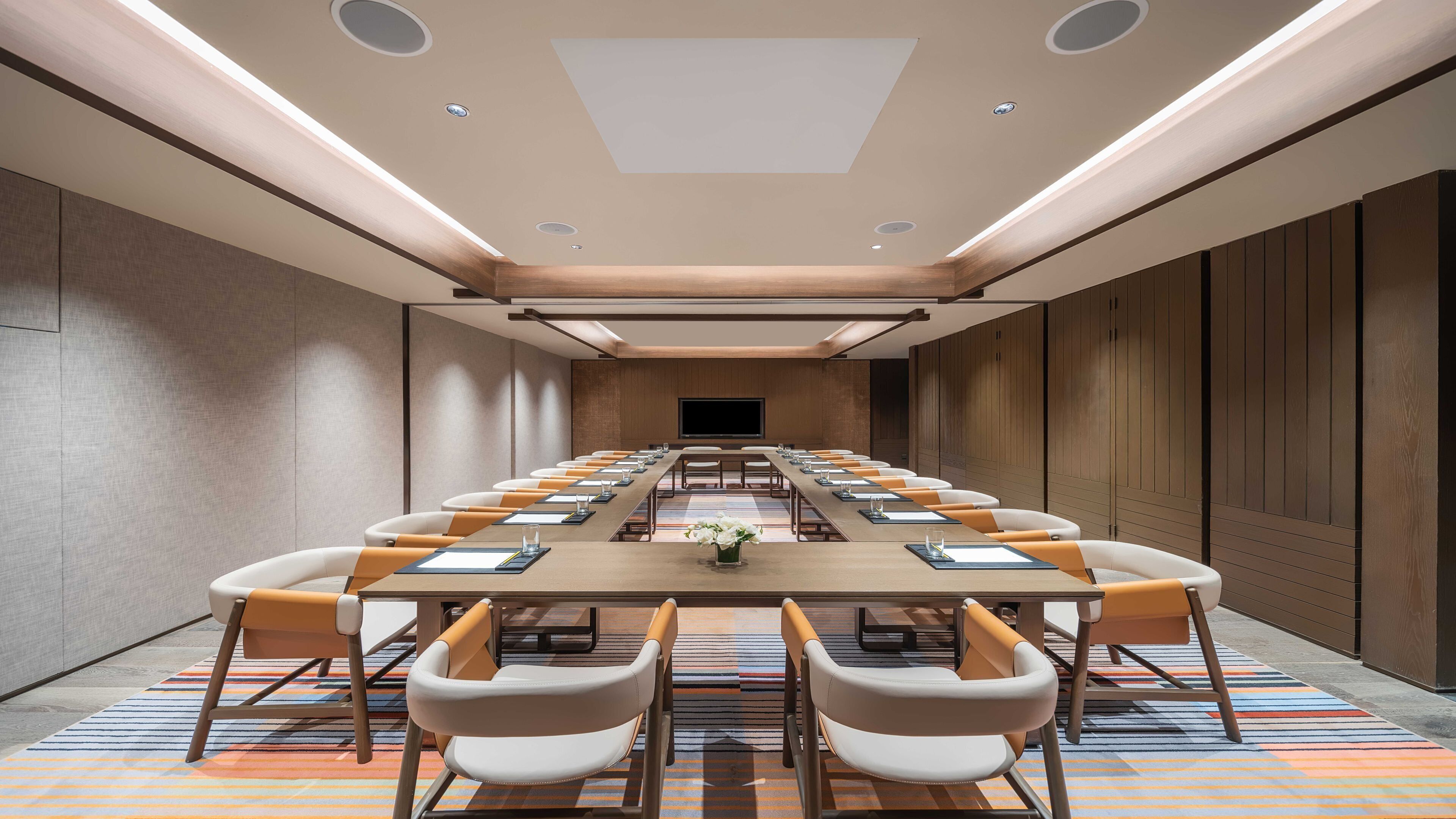 A conference room with a long table, chairs, and a television screen.