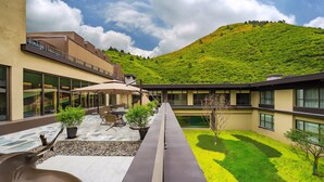 A hotel courtyard with outdoor seating, a pool, and a view of a green hillside.