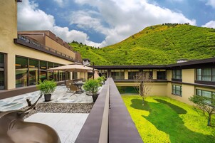 Patio de hotel con mobiliario exterior, piscina y vistas a una ladera verde.