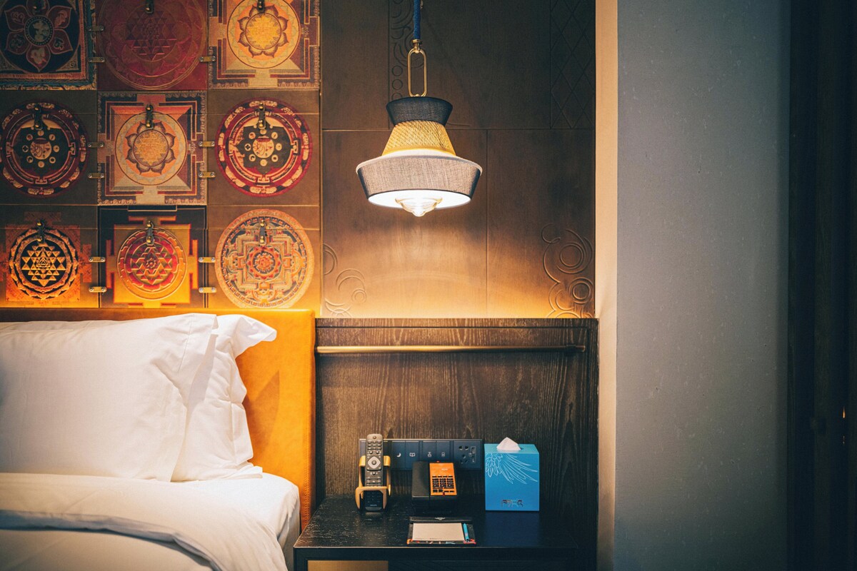 Ein Hotelzimmer mit Bett, Nachttisch mit Lampe, Fernbedienung, Taschentuchbox und Wanddekoration.