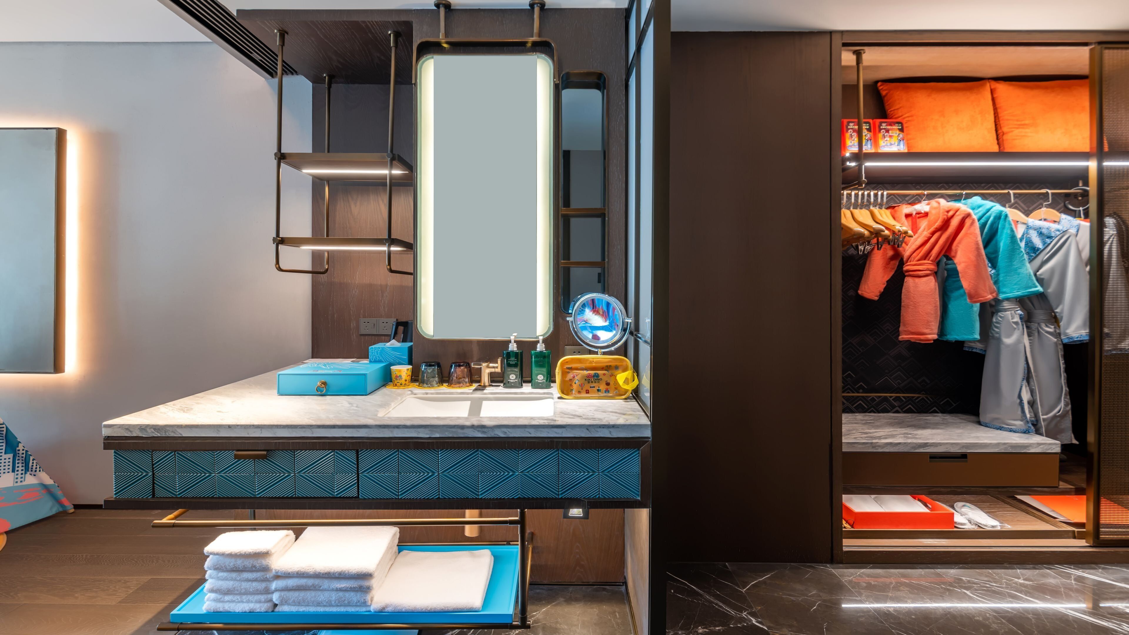 A modern bathroom with a vanity, mirror, towel rack, and a clothing storage area.