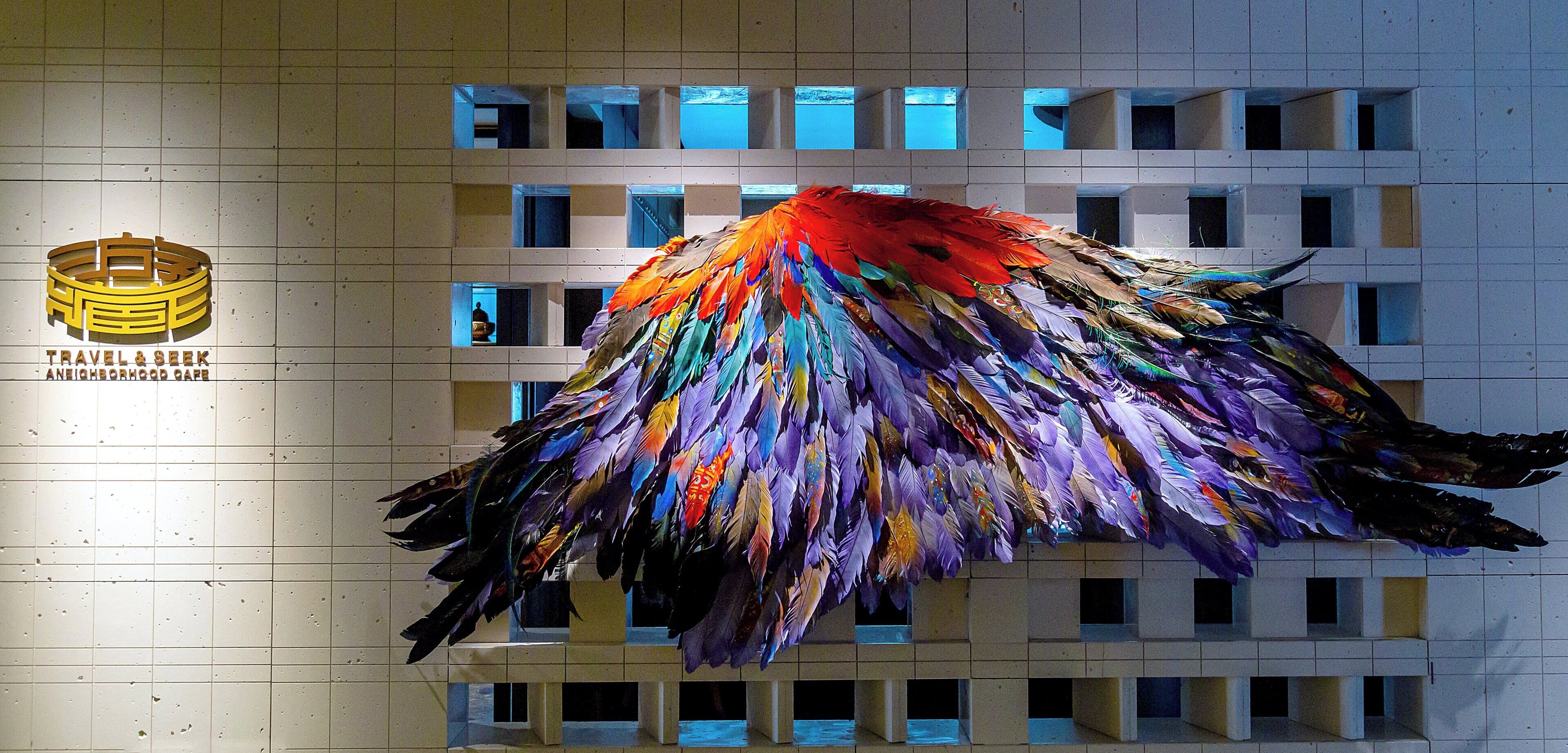 A building facade with a colorful bird sculpture and a logo for 'Travel & Seek Neighborhood Cafe'.