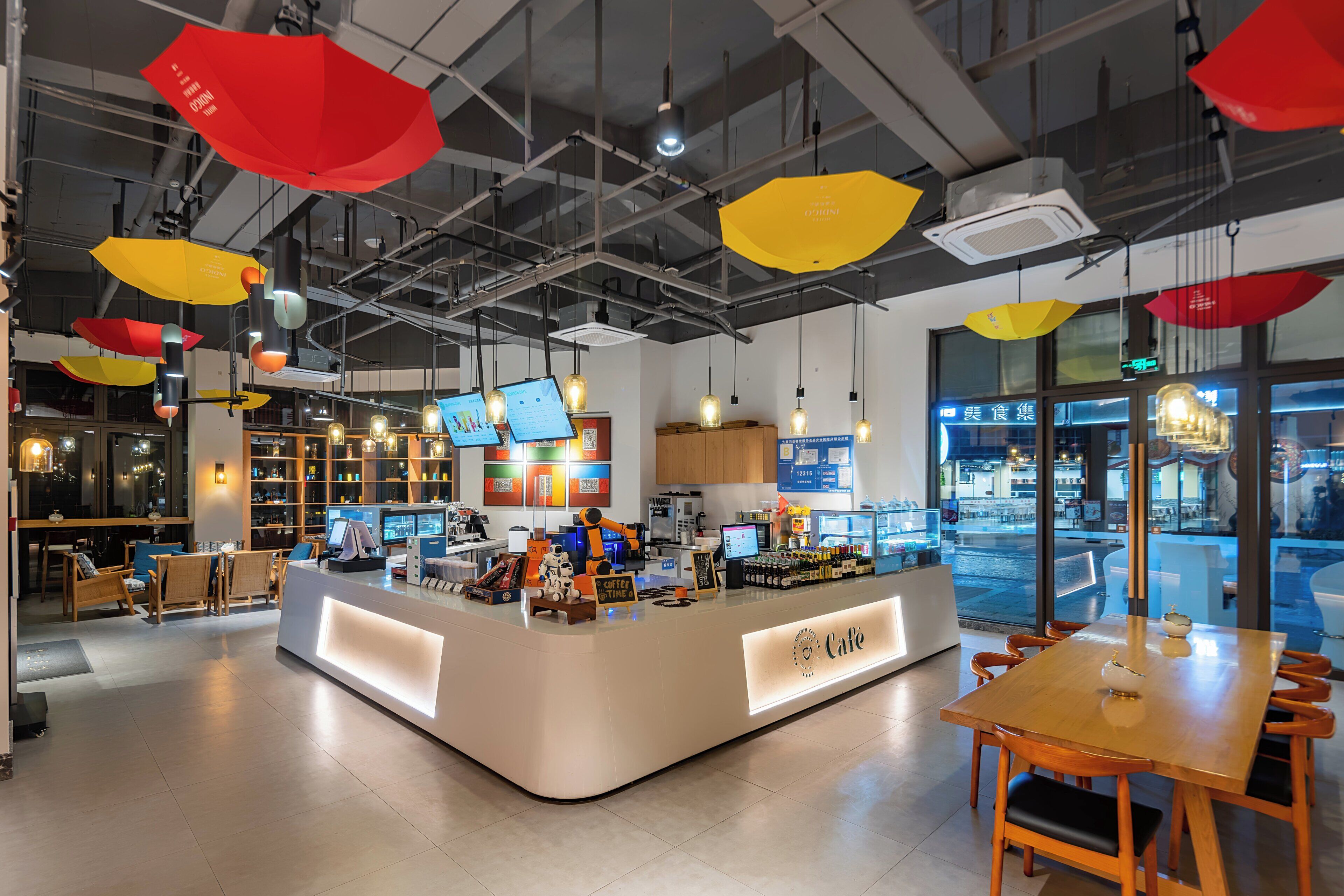 A modern cafe interior with a central counter, seating area, and hanging pendant lights.