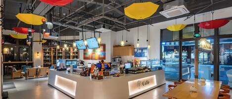 A modern cafe interior with a central counter, seating area, and hanging pendant lights.