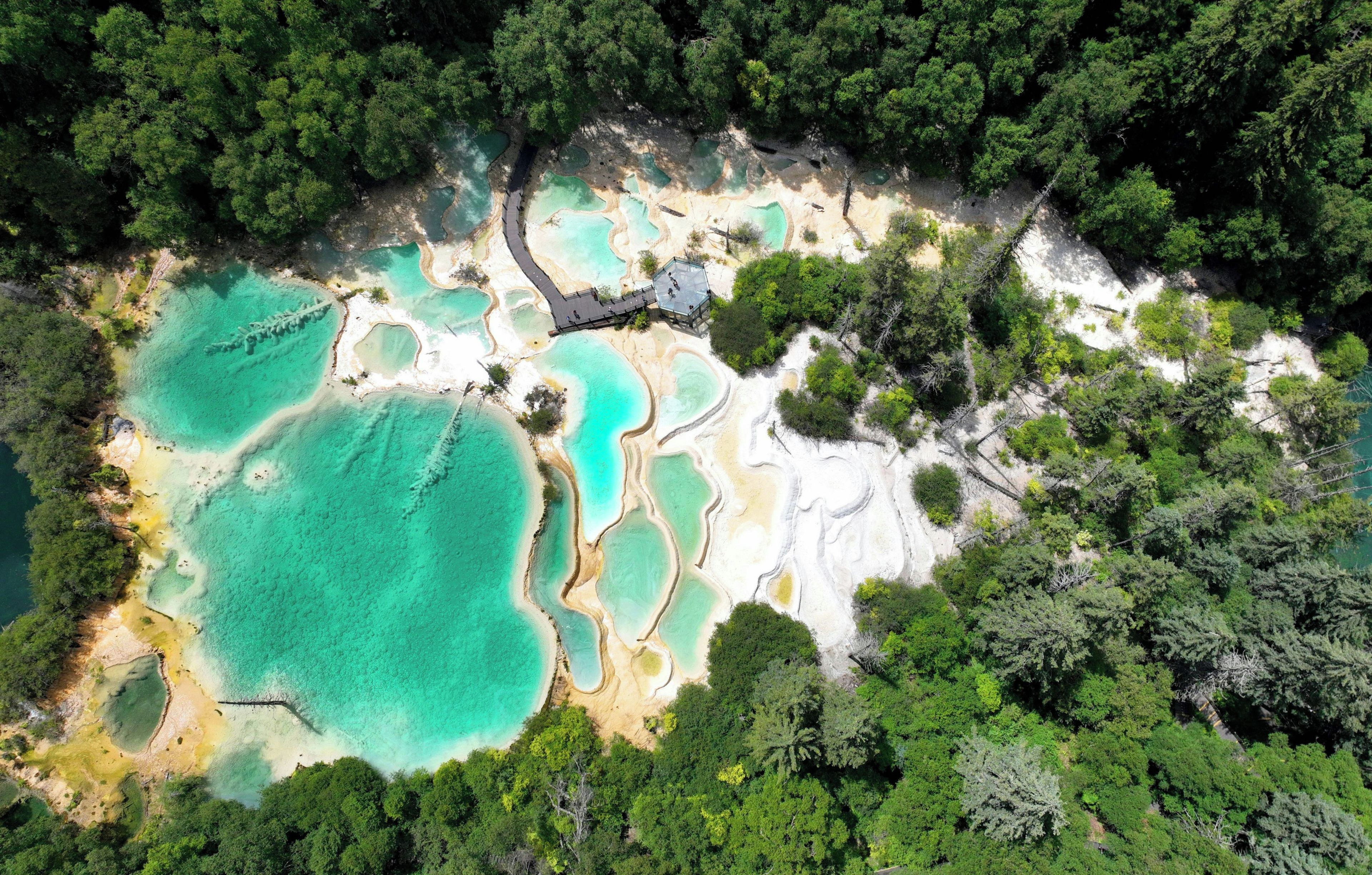 Vista aèria d'una zona de fonts termals naturals amb piscines turquesa cristal·lines, envoltades per un bosc dens.