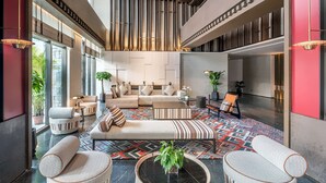 Um hall amplo com design moderno, apresentando uma área de estar central com sofás e poltronas, piso estampado e grandes janelas que permitem a entrada de luz natural.