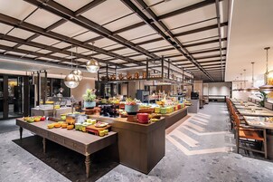 Un restaurante espacioso con techo alto, iluminación moderna y una isla central con diversos platos y utensilios.