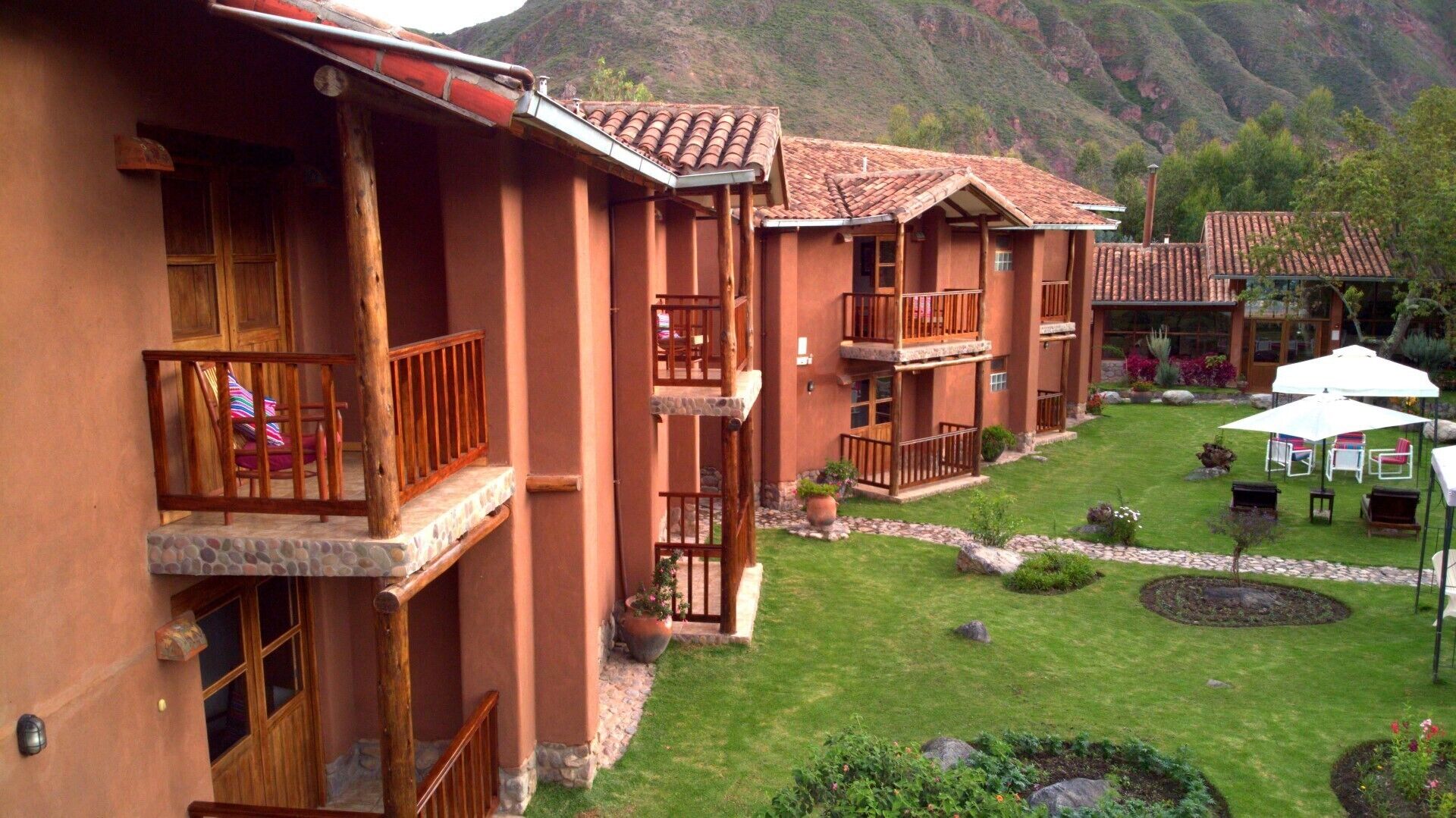 A row of terraced bungalows with balconies, a well-maintained lawn, and a mountainous backdrop.
