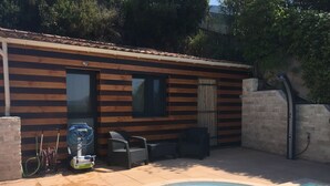 Un área de piscina con una cabaña de madera, mobiliario exterior y un carrete de manguera.