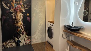 Una habitación con un mural de jirafa, una lavadora y un lavabo moderno con repisa de madera.