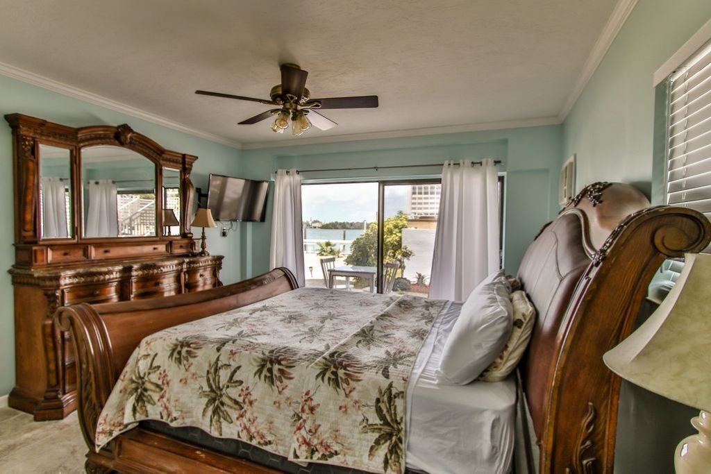 A bedroom with a wooden bed, a ceiling fan, a large mirror, and a view of the outdoors.
