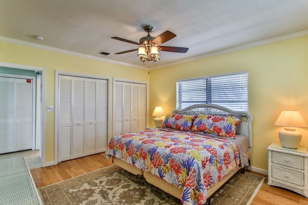 A bedroom with a bed, a ceiling fan, a window with blinds, and a nightstand with a lamp.