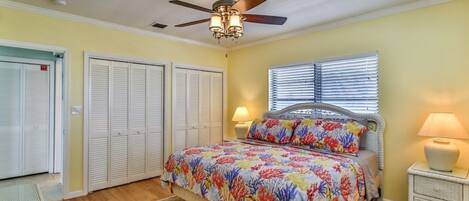 A bedroom with a bed, a ceiling fan, a window with blinds, and a nightstand with a lamp.