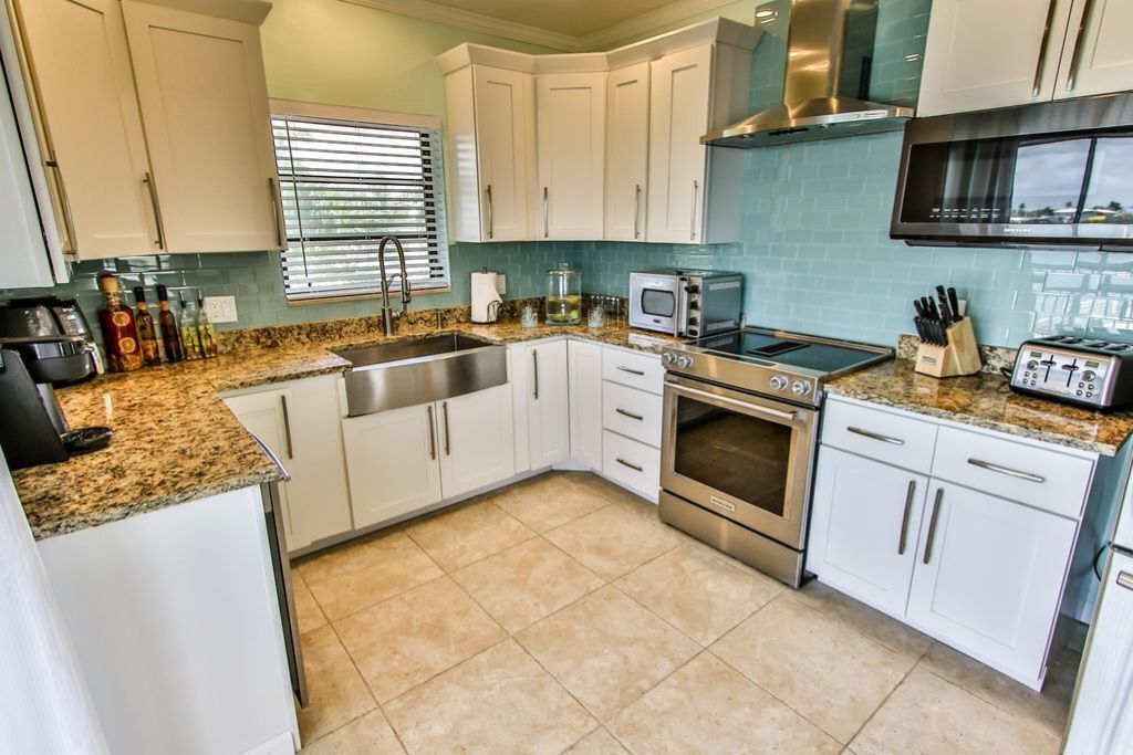 A modern kitchen with white cabinets, a granite countertop, stainless steel appliances, and a window with blinds.