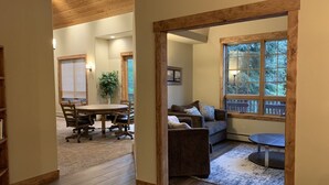 A spacious living area with a wooden ceiling, a dining table with chairs, a sofa, and a large window with a view of trees.