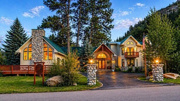 A large, two-story lodge with a stone chimney, a wrap-around porch, and a flagpole.