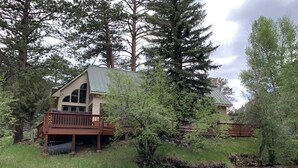 A lodge with a deck overlooking a river, surrounded by trees.
