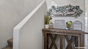 Un escalier orné d’une pancarte « Soyez les bienvenus », une petite table avec une plante, une cage à oiseaux et un vase rempli de fleurs.