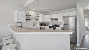 Une cuisine moderne avec des meubles blancs, un îlot central doté de tabourets, un réfrigérateur en acier inoxydable et un four encastré.