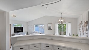 Une cuisine spacieuse avec des meubles blancs, un grand îlot central et une vue sur l’extérieur.