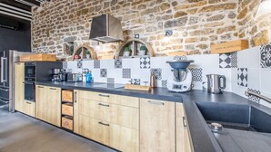 Una cocina con pared de piedra, armarios de madera, encimera negra y cafetera.