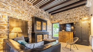 Una habitación con paredes de piedra, un sofá de cuero, un mueble de madera con placas, un televisor y una silla.