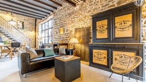 Un interior acogedor con una pared de piedra, un sofá de cuero negro, una mesa de centro trenzada y una silla de mimbre.