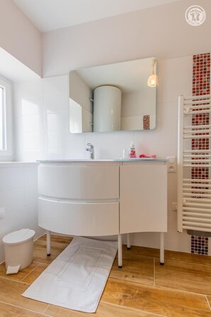 Et moderne badeværelse med et hvidt håndvaskarrangement, et spejl og en håndklædestang.