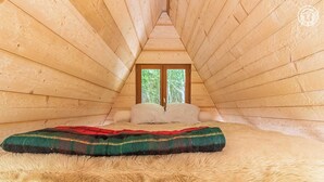 Une chambre mansardée chaleureuse avec des murs en bois, une fenêtre et un lit agrémenté d’un tapis moelleux et d’une couverture colorée.
