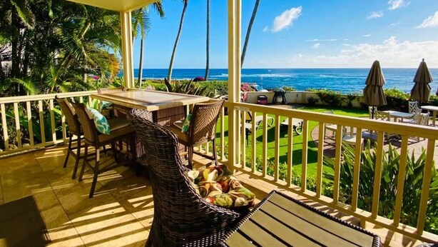 Ein überdachter Außenbereich mit Tisch und Stühlen, der Blick auf das Meer und Palmen bietet.