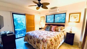 Ein Schlafzimmer mit einem Bett, einem Deckenventilator, einem Fernseher, einem Schreibtisch und einem Fenster mit Jalousien.