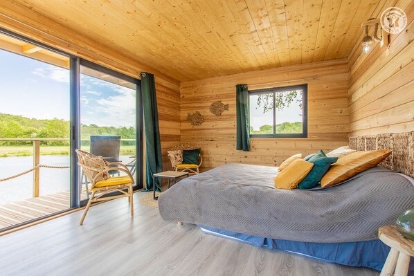 Relax in a serene space with a large bed, wooden walls, and a scenic view of greenery.