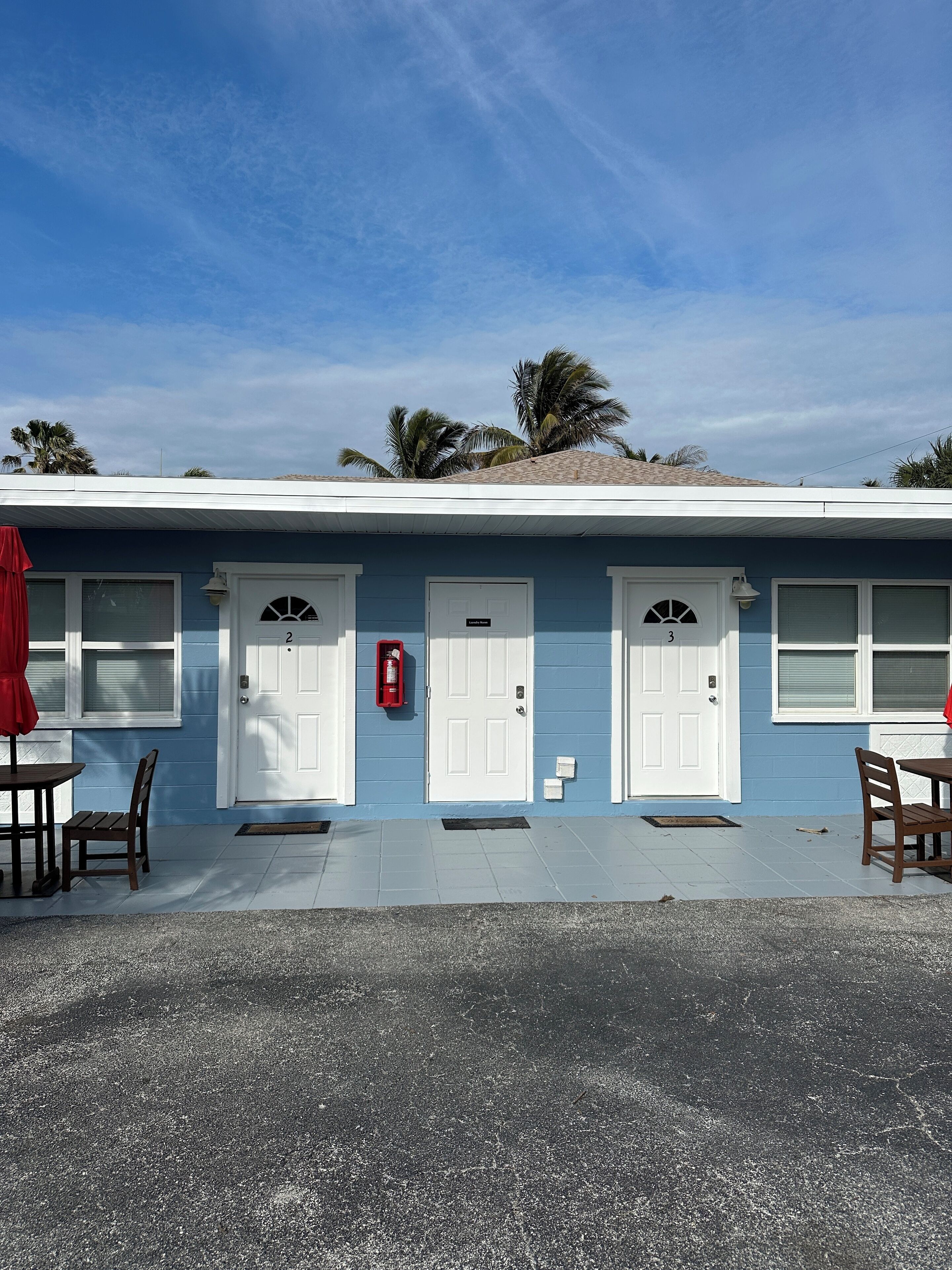 A two-story building with a blue exterior, three white doors, and a red fire extinguisher mounted on the wall.