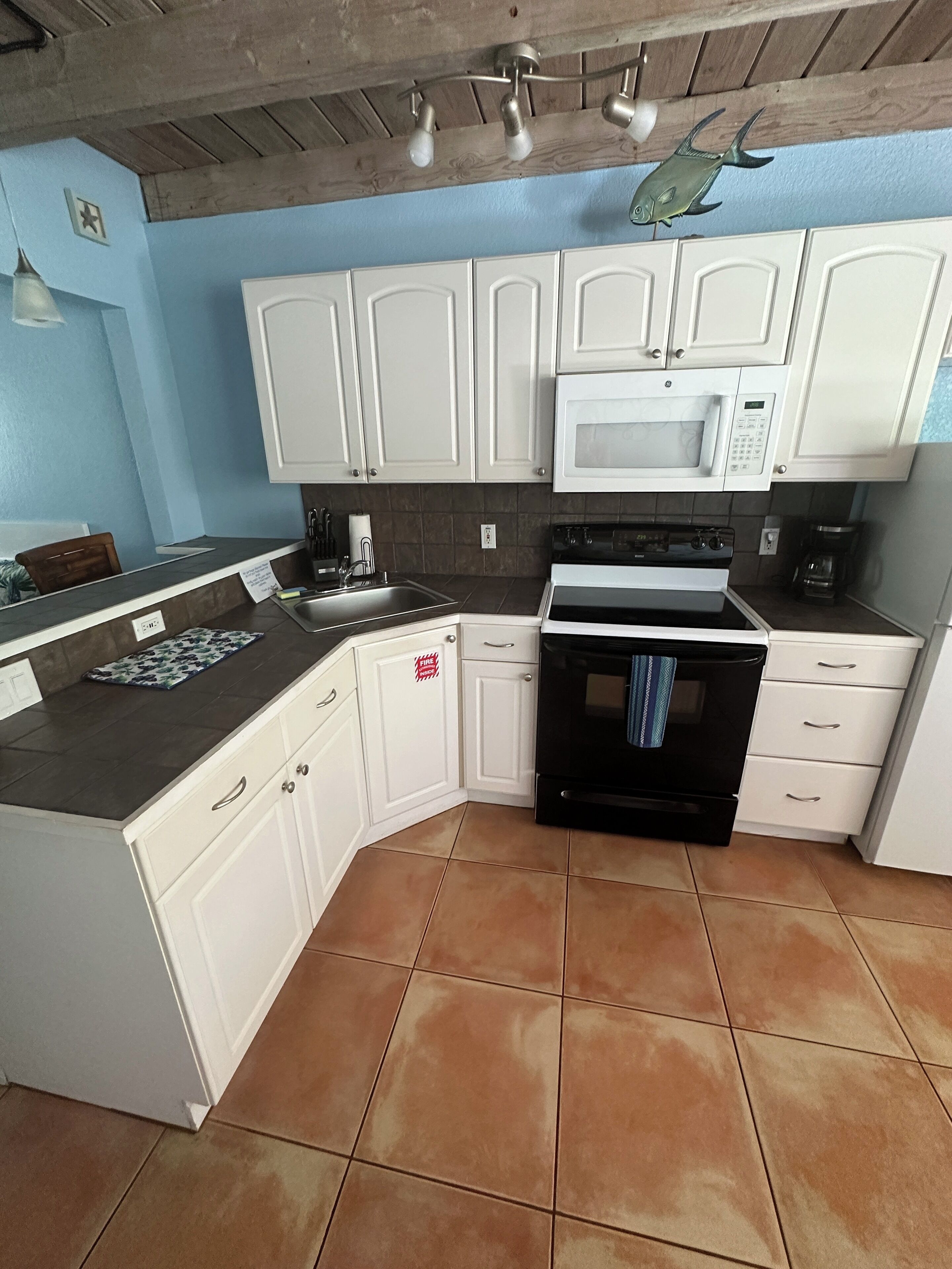 A kitchen with white cabinets, a black stove, a microwave, and a tiled floor.