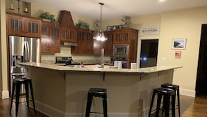 A modern kitchen with wooden cabinets, stainless steel appliances, and a central island with bar stools. - Huge 4 bedroom + loft lakehouse with private dock - 27 min north of Sundance Sq  (Fort Worth)