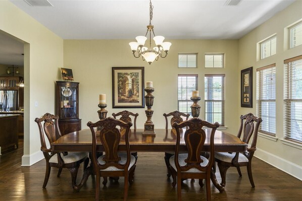 A dining room with a large wooden table and chairs, a chandelier, and framed artwork on the walls.