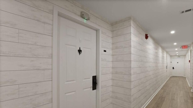 A hallway with white doors, a light-colored wooden floor, and a white wall with a subtle texture. - Port Royal Village 302 - Walk to Beach (Hilton Head Island)