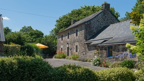 A stone house with a steeply pitched roof, surrounded by lush greenery and a small patio area with outdoor seating.
