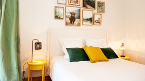 A neatly arranged bedroom with a bed, pillows, a nightstand, a lamp, and a wall with framed pictures.