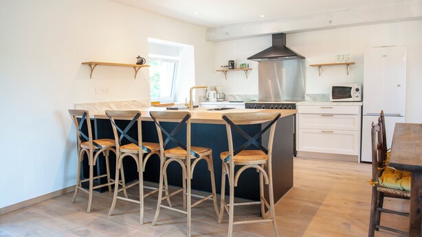 A modern kitchen with a central island, bar stools, a stove, microwave, and a refrigerator.