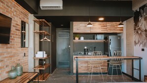 A compact kitchen with wooden cabinets, a countertop, and a refrigerator. There are two chairs and a hanging light fixture. - Cost-effective enjoyable Studio in Laureles with A/C (Medellín)