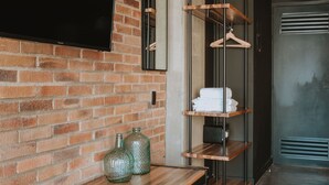 A modern hotel room with a brick wall, a flat-screen TV mounted above a wooden bench, and a metal shelving unit with hangers. - Cost-effective enjoyable Studio in Laureles with A/C (Medellín)