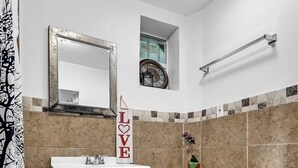 A bathroom with a white sink, a toilet, a mirror, a clock, and a 'LOVE' sign.