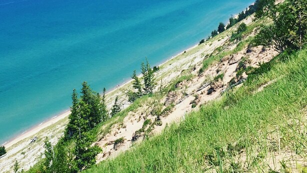 A coastal landscape with a clear view of the ocean, a sandy beach, and a grassy hillside. - Lakefront cottage on Secluded Upper Herring Lake (Frankfort)