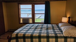 A hotel room with a bed, a window with a view of a body of water and a dock, and a bedside lamp. - Lakefront cottage on Secluded Upper Herring Lake (Frankfort)