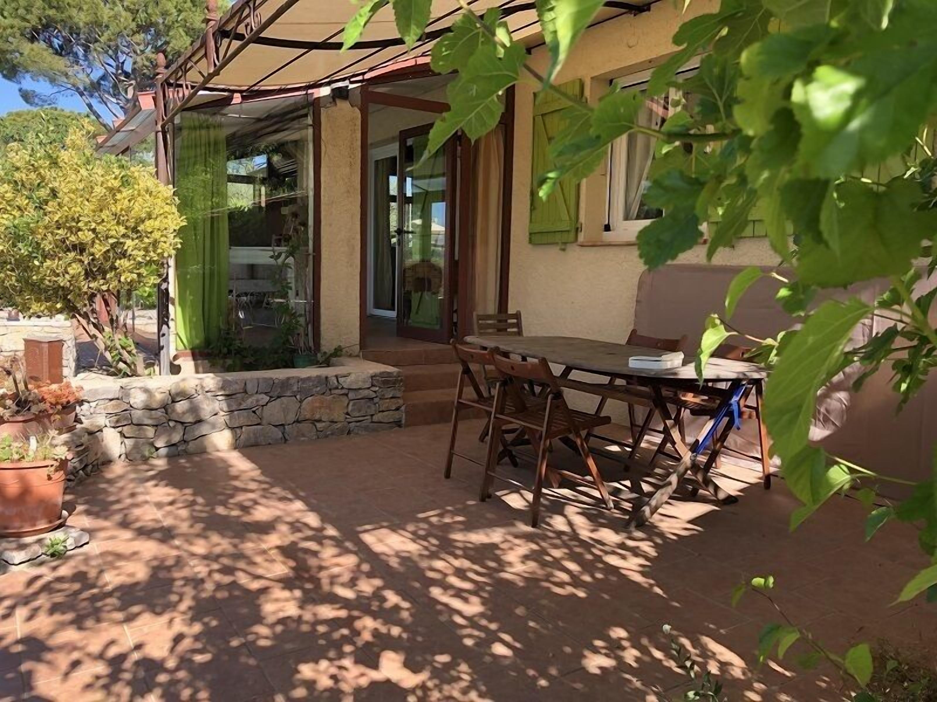 Eine Terrasse im Freien mit Tisch und Stühlen, umgeben von Steinmauern und Kübelpflanzen.