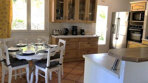 A kitchen with wooden cabinets, a dining table set for four, a coffee maker, and a refrigerator. - Gîte de Font du Roux (FLAYOSC)